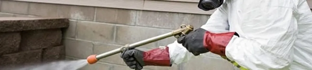 Pest control technician applying exterior insect treatment along a home foundation in Manchester, NH