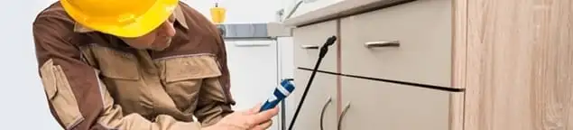 Roach exterminator applying treatment under kitchen cabinets in Manchester, NH
