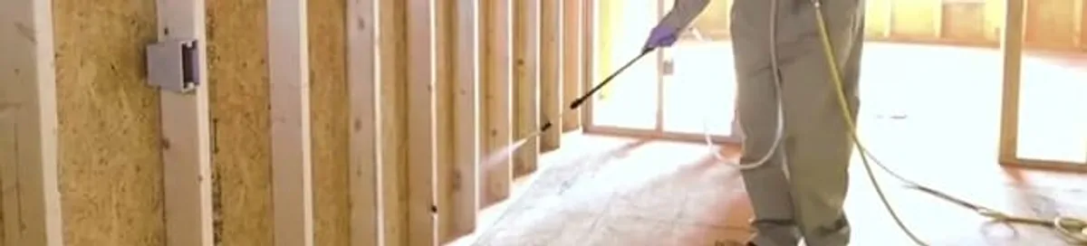 Termite treatment technician applying spray along framing and unfinished walls in Manchester, NH