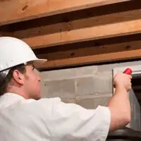 Termite inspection technician checking a basement wall and framing for termite activity in Manchester, NH